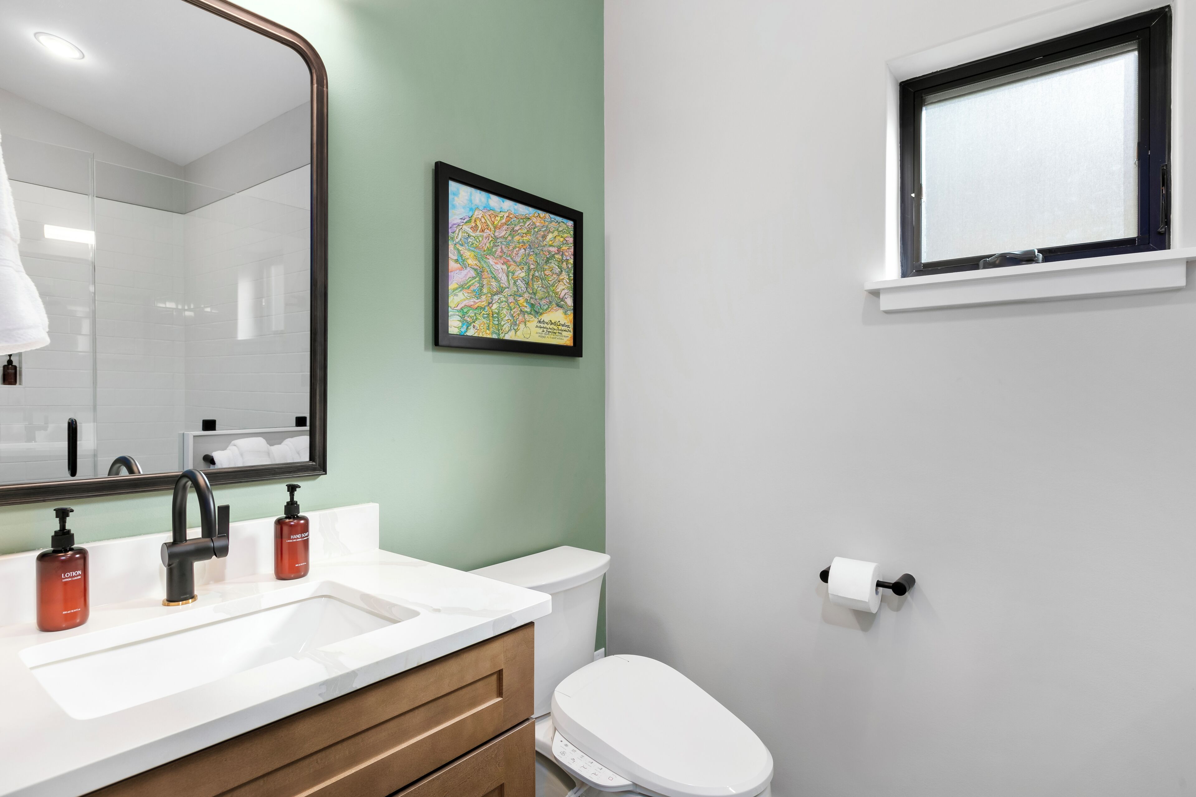 A bathroom with a white sink, a mirror, a toilet, and a window.