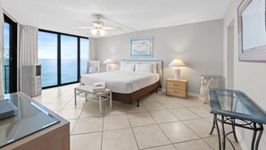 Een moderne hotelkamer met een groot bed, nachtkastjes, een glazen bureau en uitzicht op zee.