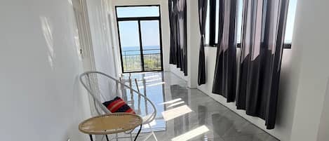 A spacious hallway with a modern design, featuring a glossy tiled floor, a wicker chair, and a large window with curtains.