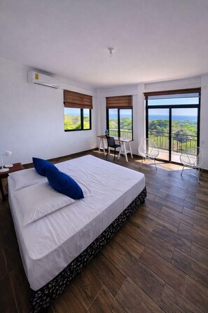 Een slaapkamer met een groot bed, een bureau en een balkon met uitzicht.