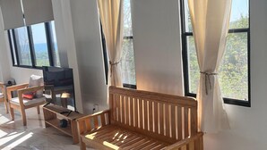 Une pièce avec un banc en bois, un téléviseur et de grandes fenêtres avec des rideaux.