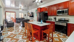 A spacious kitchen with wooden cabinets, a large island with chairs, a refrigerator, microwave, stove, and a ceiling fan. - Spacious 5-bedroom house in welcoming Managua with WiFi, AC (Managua)