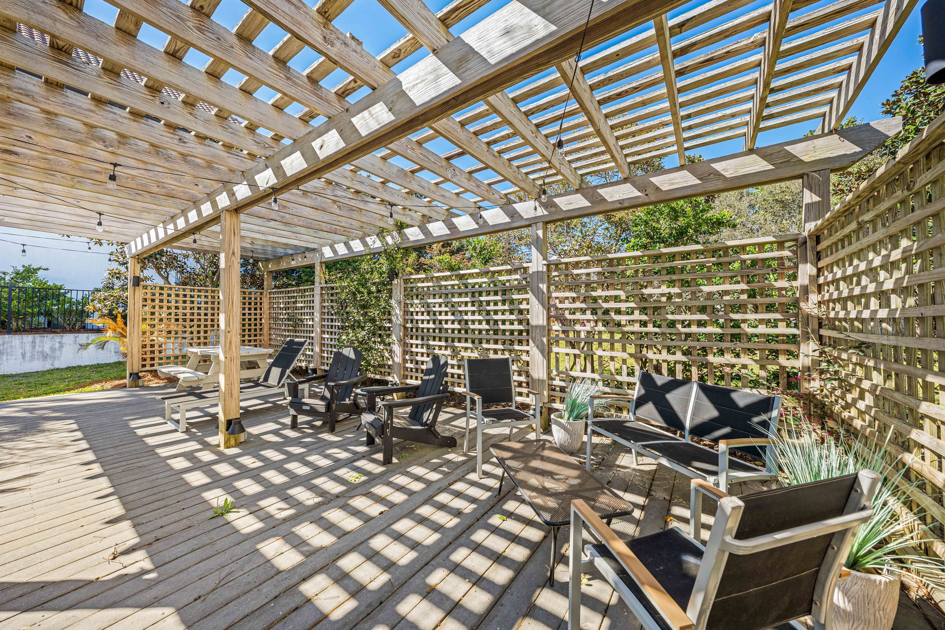 An outdoor patio with wooden pergola, seating, and potted plants.