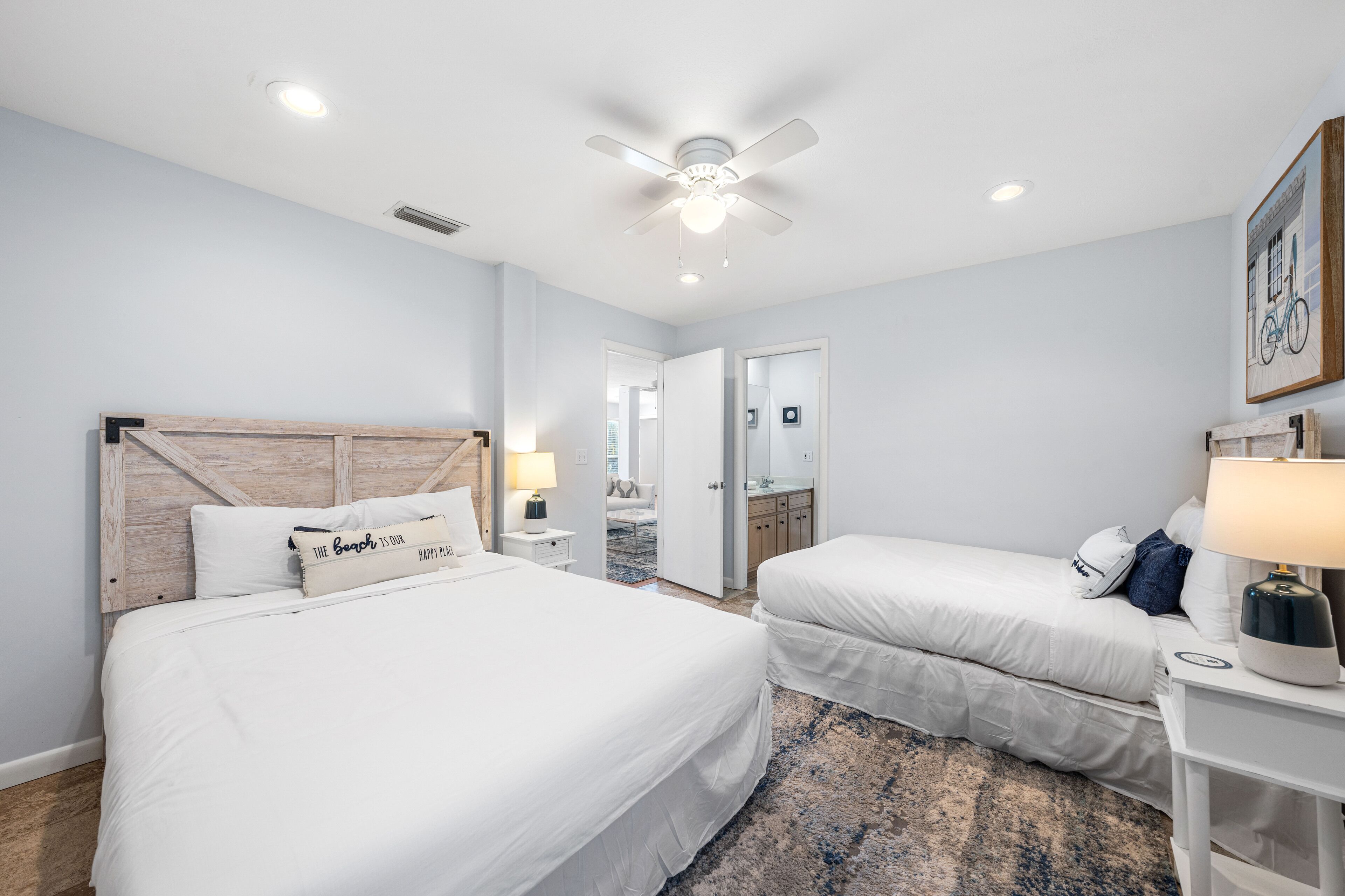 Une chambre d’hôtel avec deux lits, un ventilateur de plafond, une table de chevet avec une lampe et une porte donnant sur une salle de bain.