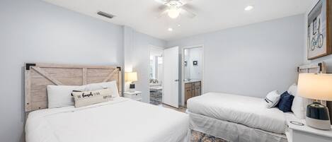 A hotel room with two beds, a ceiling fan, a nightstand with a lamp, and a door leading to a bathroom.