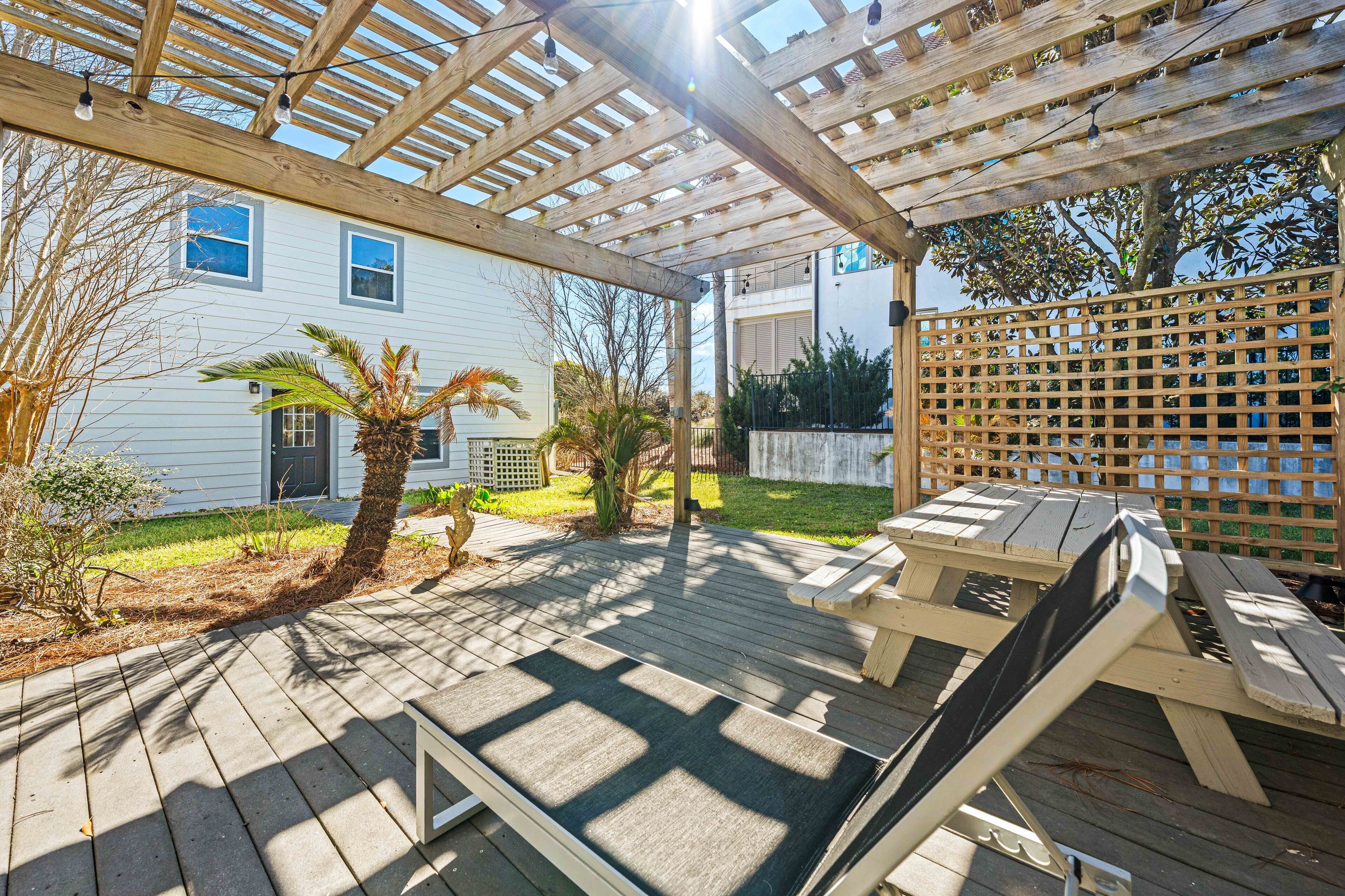 A wooden deck with a pergola, outdoor seating, and a view of a white house.