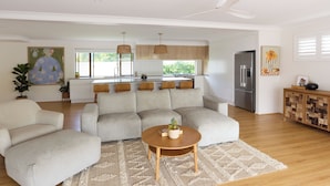 Una sala moderna con un sofá modular, una mesa de centro redonda y una cocina al fondo.
