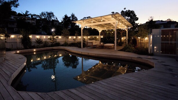 Una piscina con terraza de madera y zona de estar cubierta con luces colgantes.