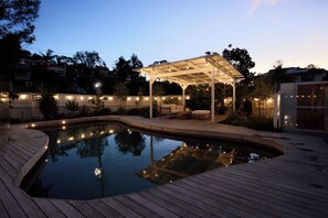 Una piscina con terraza de madera y zona de estar cubierta con luces colgantes.