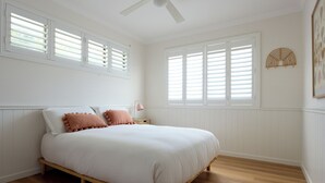 Un dormitorio con cama de madera, paredes blancas y suelo de madera.