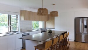 Una cocina moderna con una isla grande, muebles blancos, electrodomésticos de acero inoxidable y taburetes de madera.