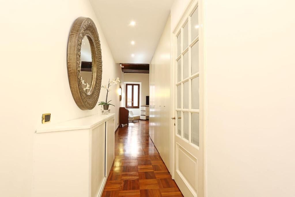 A hallway with a wooden floor, a large mirror on the left, and a white door on the right.
