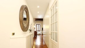 A hallway with a wooden floor, a large mirror on the left, and a white door on the right. - Riccardo Condotti Suite (Rome)