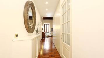 A hallway with a wooden floor, a large mirror on the left, and a white door on the right.