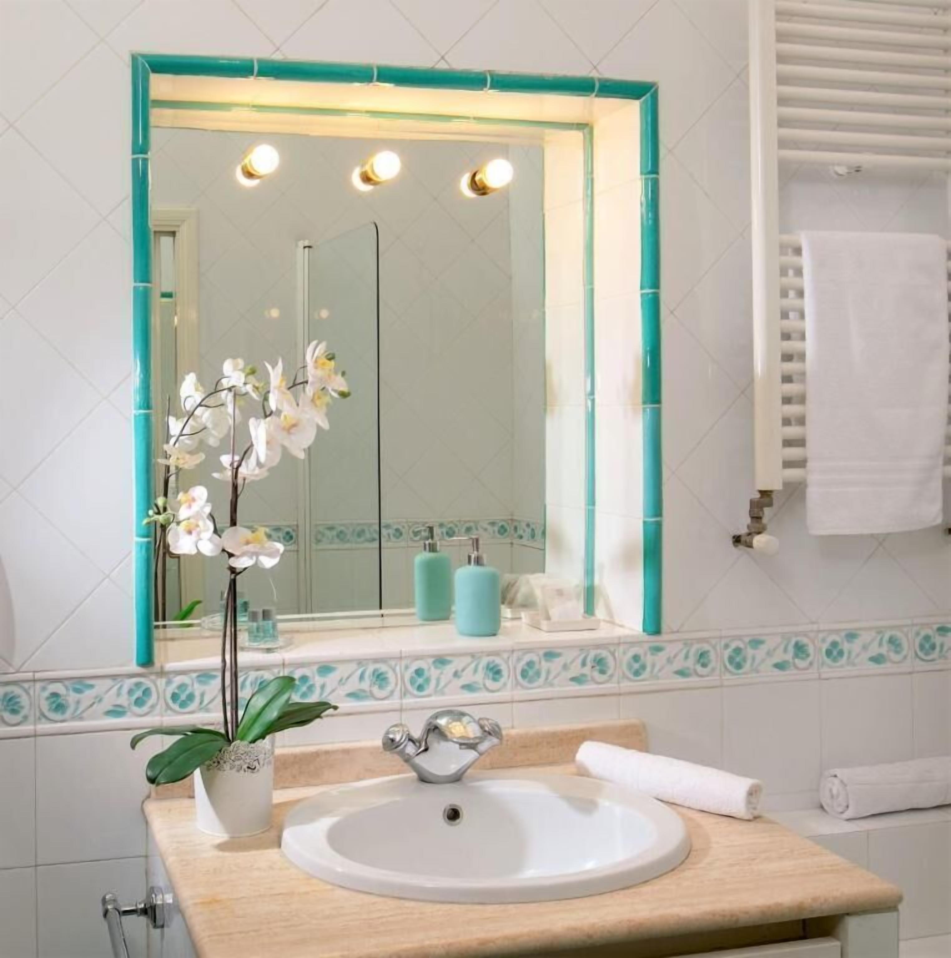 Un baño con lavamanos blanco, espejo con marco verde azulado y una orquídea en maceta.