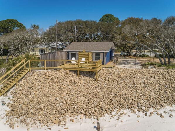 A beach house with a wooden deck, a small porch, and a sandy beach area.