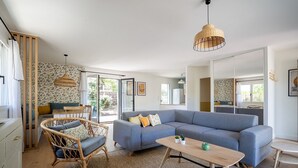 A modern living room with a blue sectional sofa, wicker chairs, a wooden coffee table, and a large mirror. - Villas Indigo, Villa(s) Indigo proches des plages (La Teste-de-Buch)