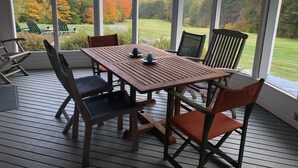A wooden deck with a table and chairs, large windows offering a view of a forested landscape.