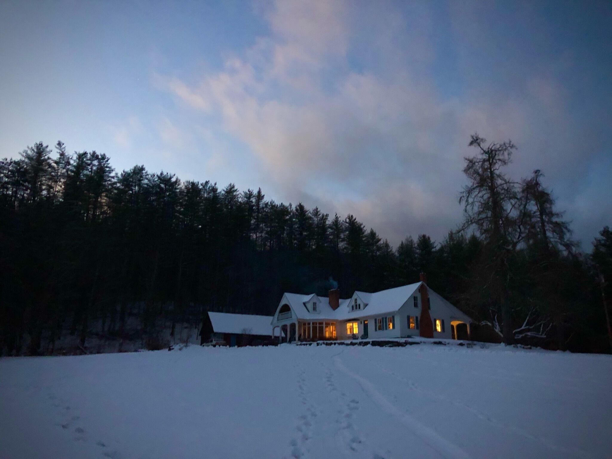 A large, snow-covered house with multiple chimneys and a snow-covered driveway.