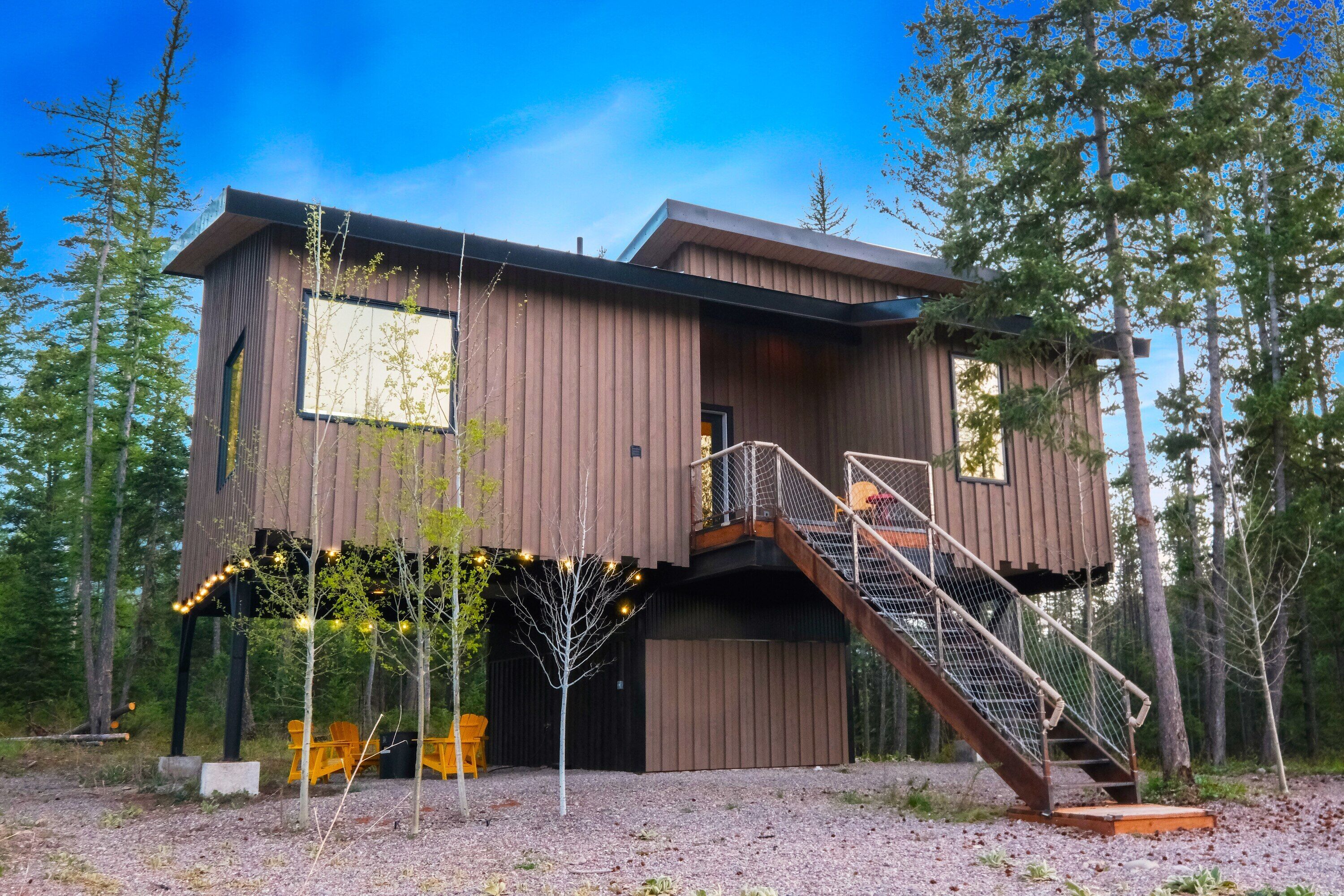 Un moderno chalet in legno con un balcone, una scala e vista sulla foresta circostante.