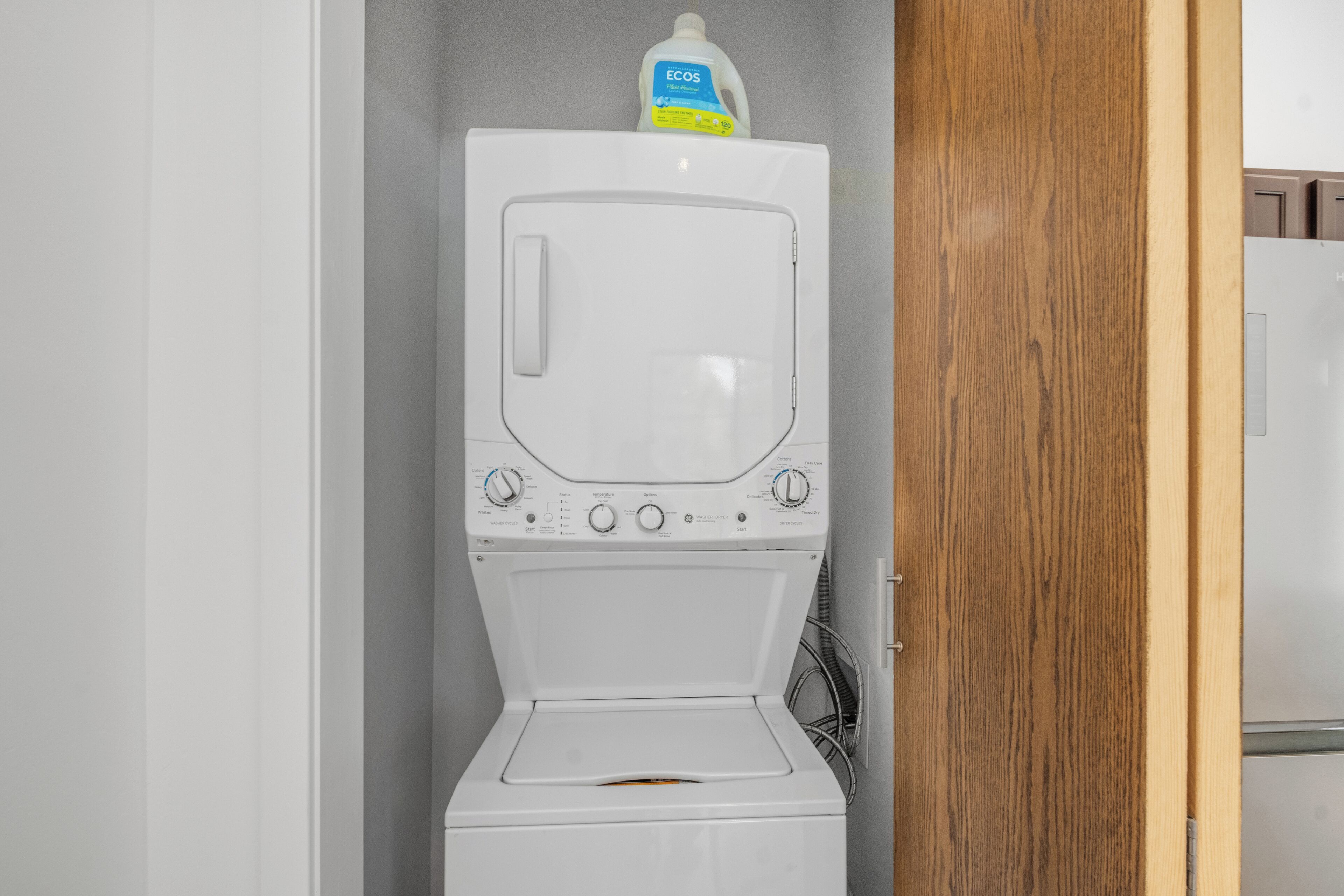 Een compacte, witte was- en droogcombinatie met bedieningspaneel en een fles wasmiddel er bovenop.