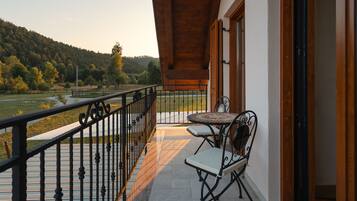 Ein Balkon mit Tisch und Stühlen, der auf eine grüne Landschaft und Hügellandschaft blickt.