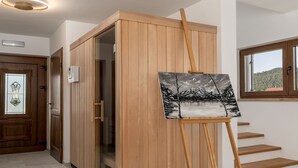 Een kamer met een houten kast, een schilderij op een ezel, een deur met een glas-in-loodraam en een raam met uitzicht op een heuvel.
