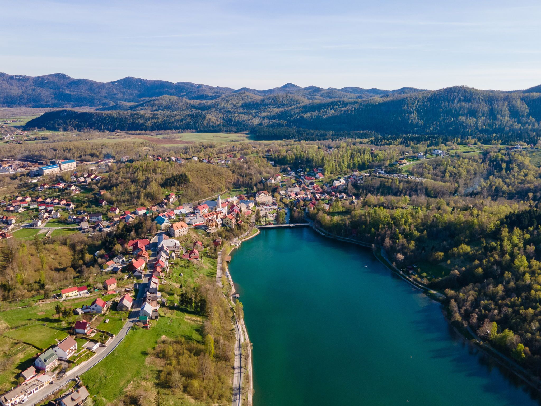 An aerial view of a lakeside town with houses, a church, and a bridge.