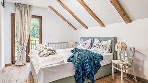 Een slaapkamer met een bed, een stoel, een raam met gordijnen en uitzicht op groen buiten.