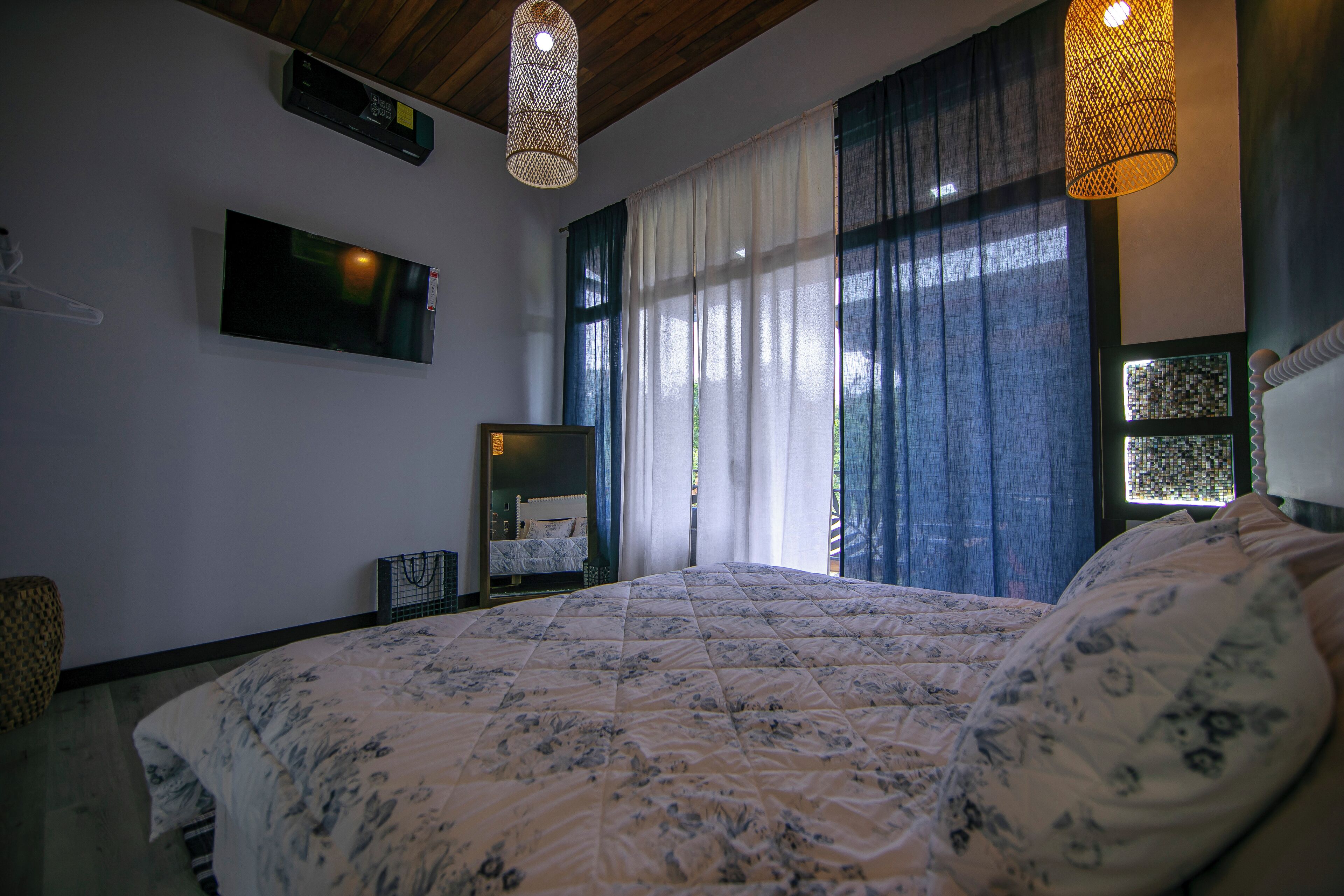 Une chambre à coucher avec un grand lit, un téléviseur fixé au mur et une fenêtre avec des rideaux.
