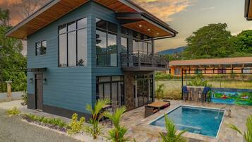 Une maison moderne à deux étages, dotée d’un grand balcon, d’une piscine et d’un jardin.