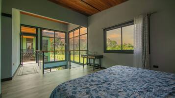 A bedroom with a large bed, a desk, and a view of the outdoors through a sliding door.