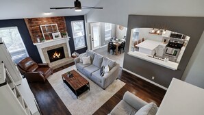 A modern living room with a fireplace, a dining area, and a kitchen with a large island.