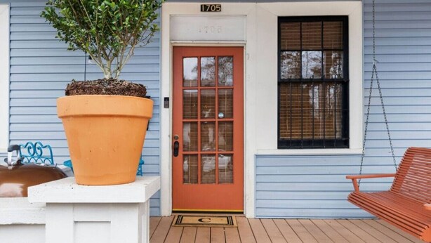A house with a wooden deck, a large potted plant, a red door, and a swing chair. - The Brass Bungalow - A Nostalgic Escape! (Birmingham)