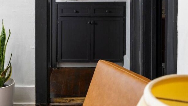 Un pasillo estrecho con un ventanal de vitrales, una puerta de madera oscura y una pared blanca.