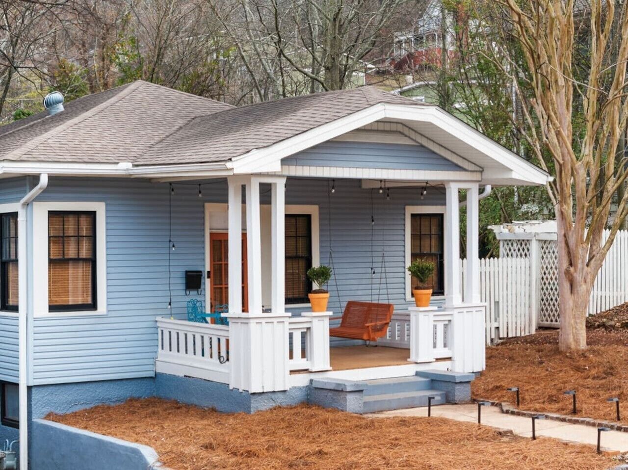 A single-story house with a porch, a swing chair, and a potted plant.