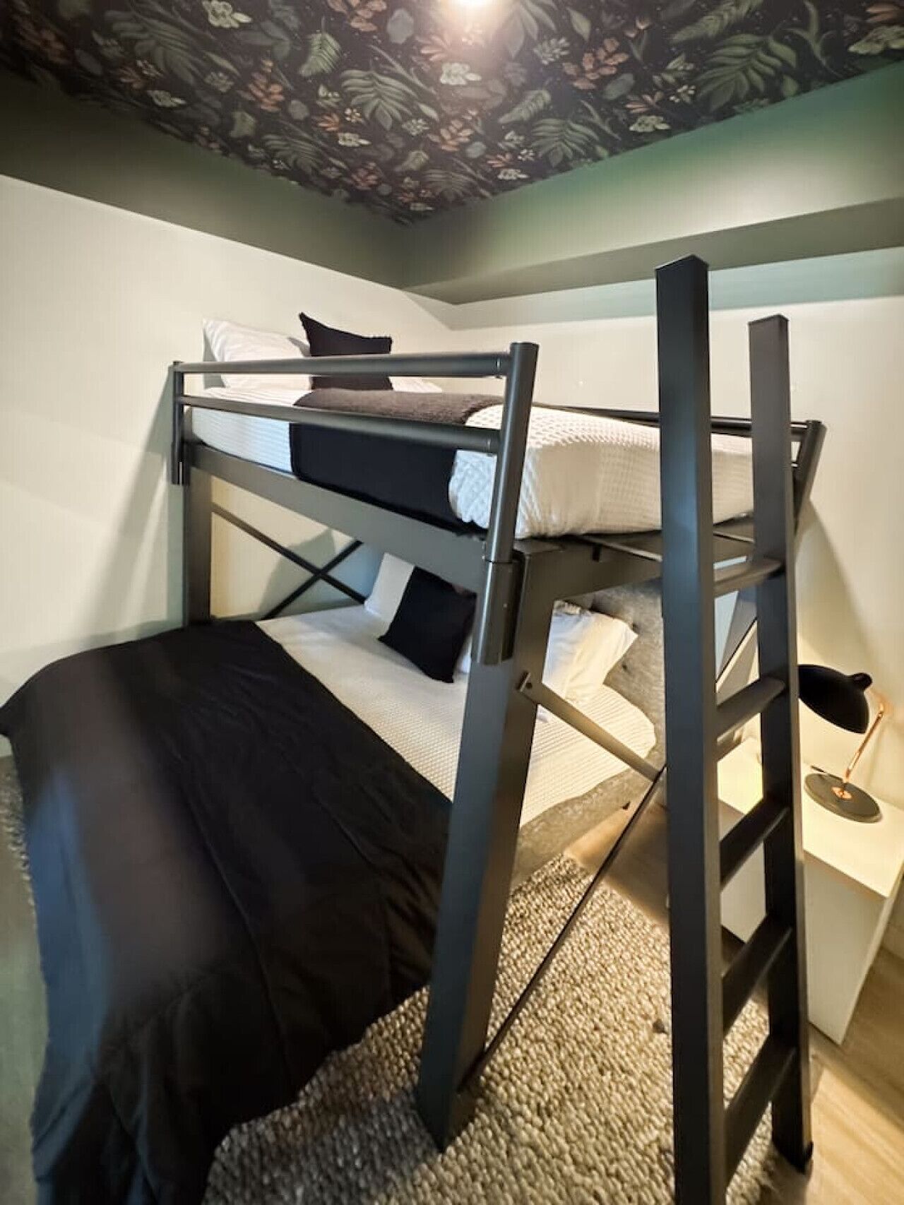 Ein Stockbett mit Schreibtisch und Stuhl, eine strukturierte Decke und ein Teppichboden.