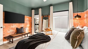 A modern bedroom with a bed, a bench, a bedside table with a tray, a ceiling fan, and a large window with curtains.