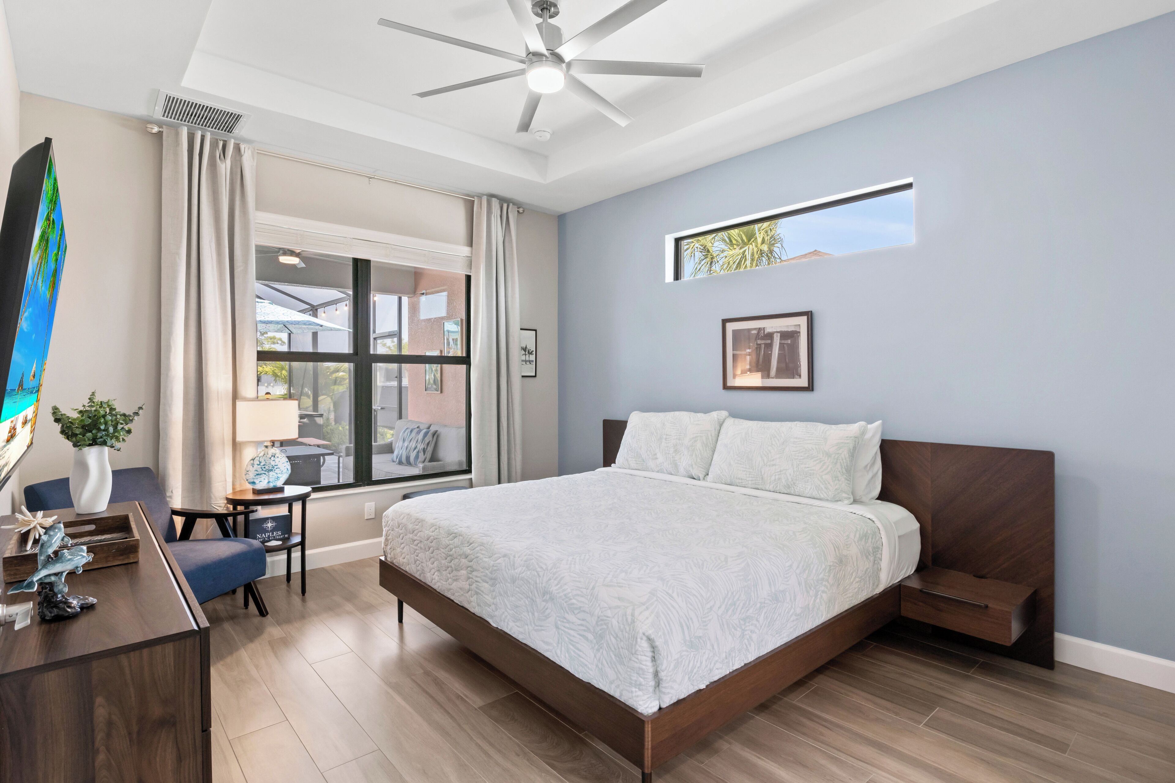 A modern bedroom with a large bed, a desk, and a window with a view of the outside.