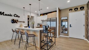Una cocina moderna con una isla central, taburetes de bar, iluminación colgante y una guitarra montada en la pared.