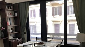 A modern living room with a dining area, large windows with curtains, a sofa, and a bookshelf. - VISCONTI APARTMENT (Rome)