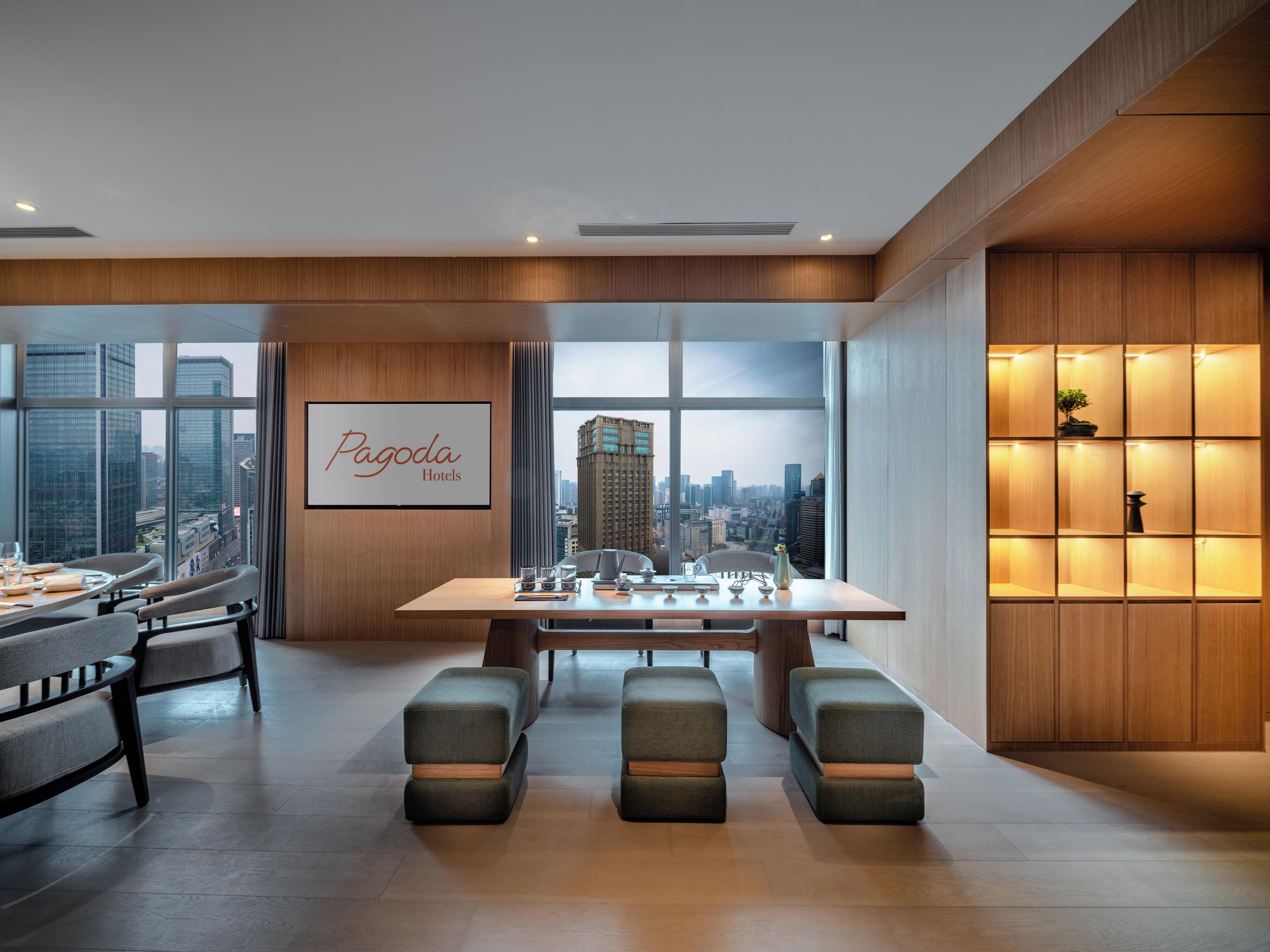 A modern hotel room with a large window offering a city view, a neatly arranged dining table, and a comfortable seating area.