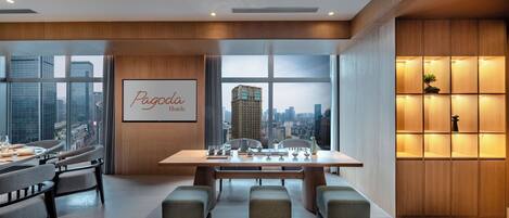 A modern hotel room with a large window offering a city view, a neatly arranged dining table, and a comfortable seating area.