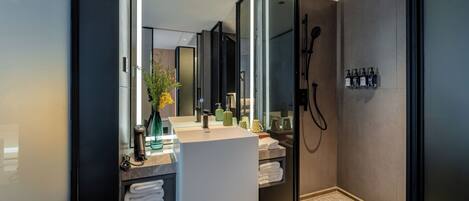 A modern bathroom with a glass shower enclosure, a large mirror, and a vanity with toiletries.