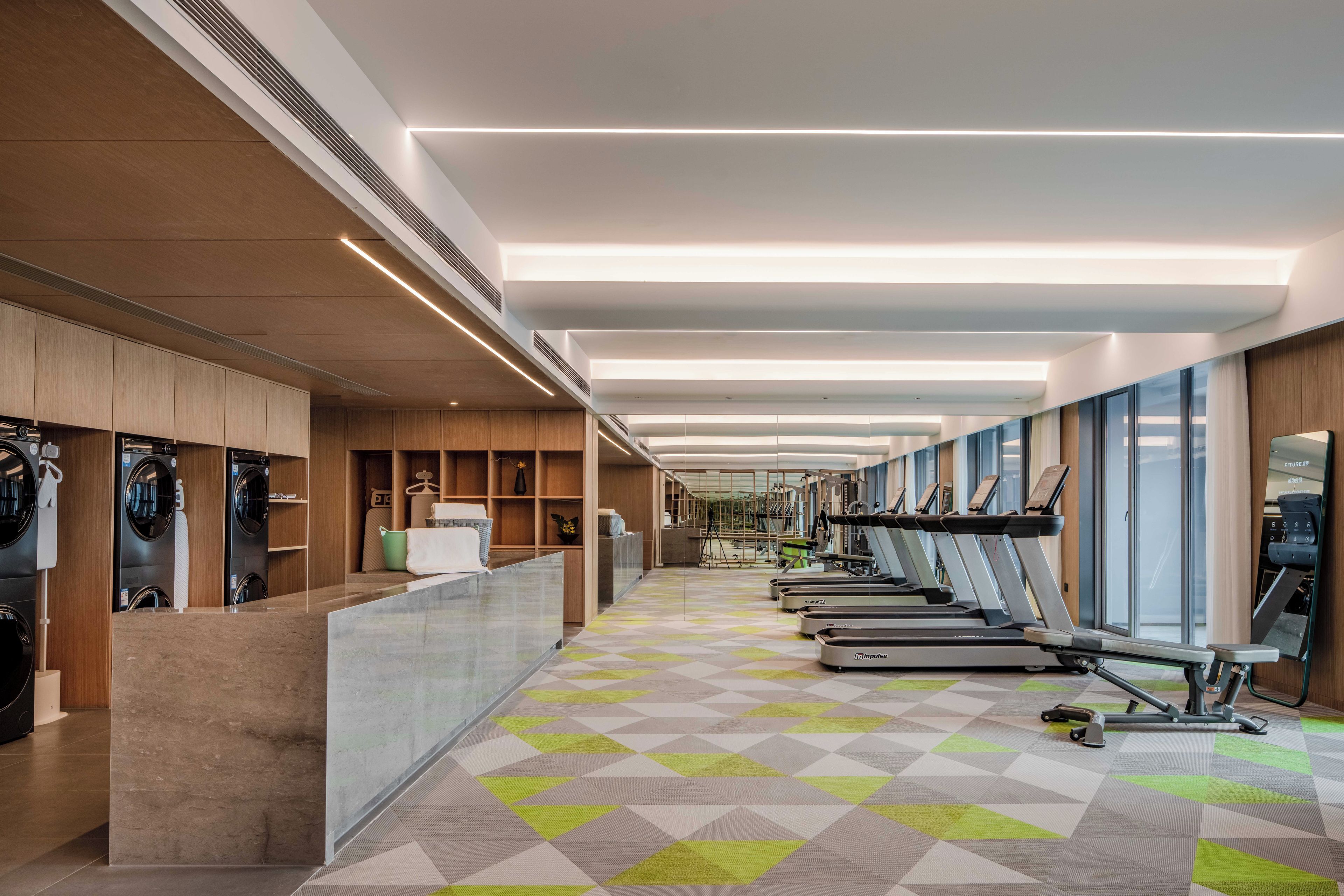 A modern gym with exercise equipment, a reception desk, and a patterned floor.