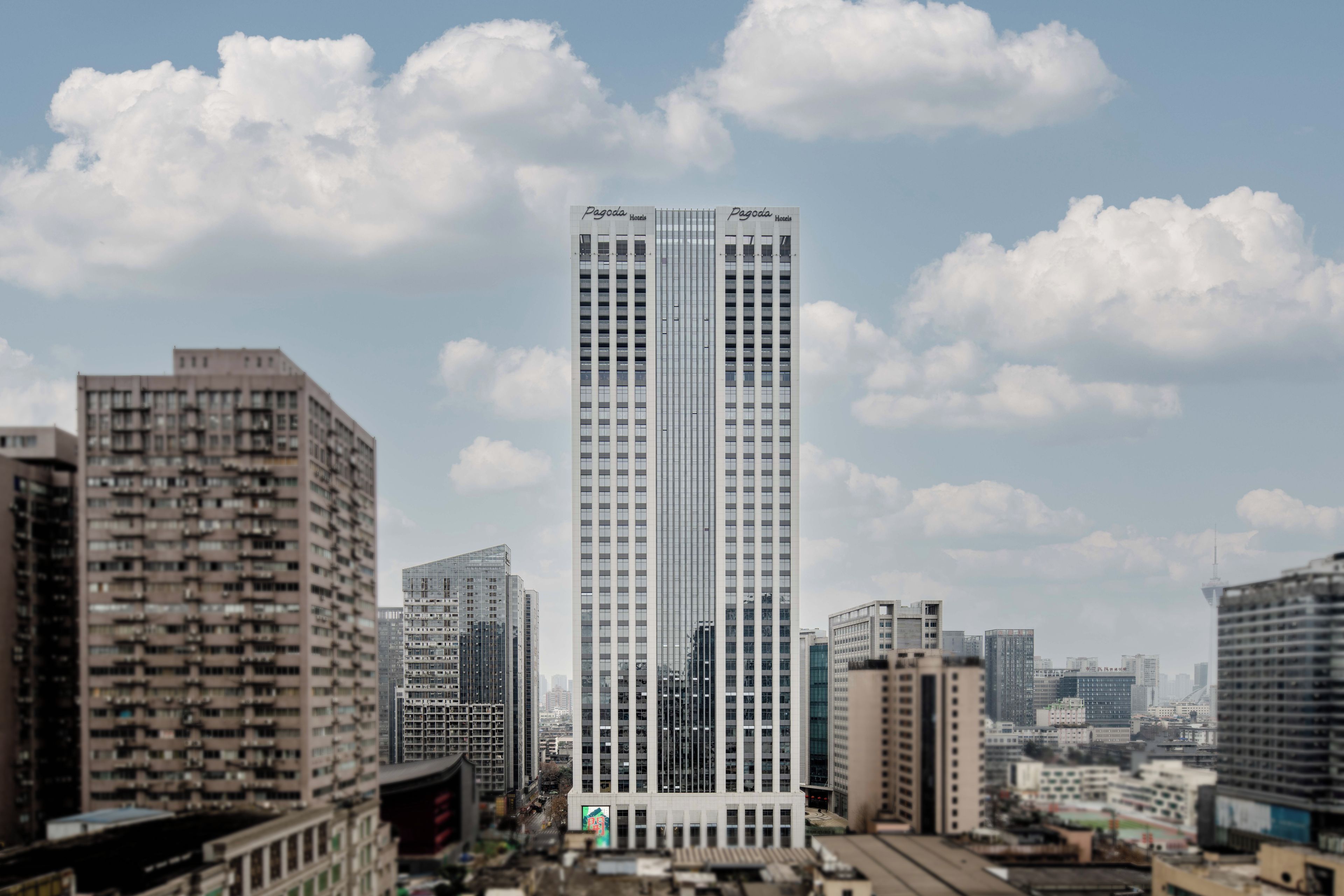 Un hôtel de grande hauteur à la façade moderne en verre, entouré d’autres immeubles de grande hauteur dans un environnement urbain.