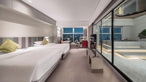 Habitación de hotel moderna con una cama grande, un escritorio y vistas de la ciudad a través de ventanales de gran altura.