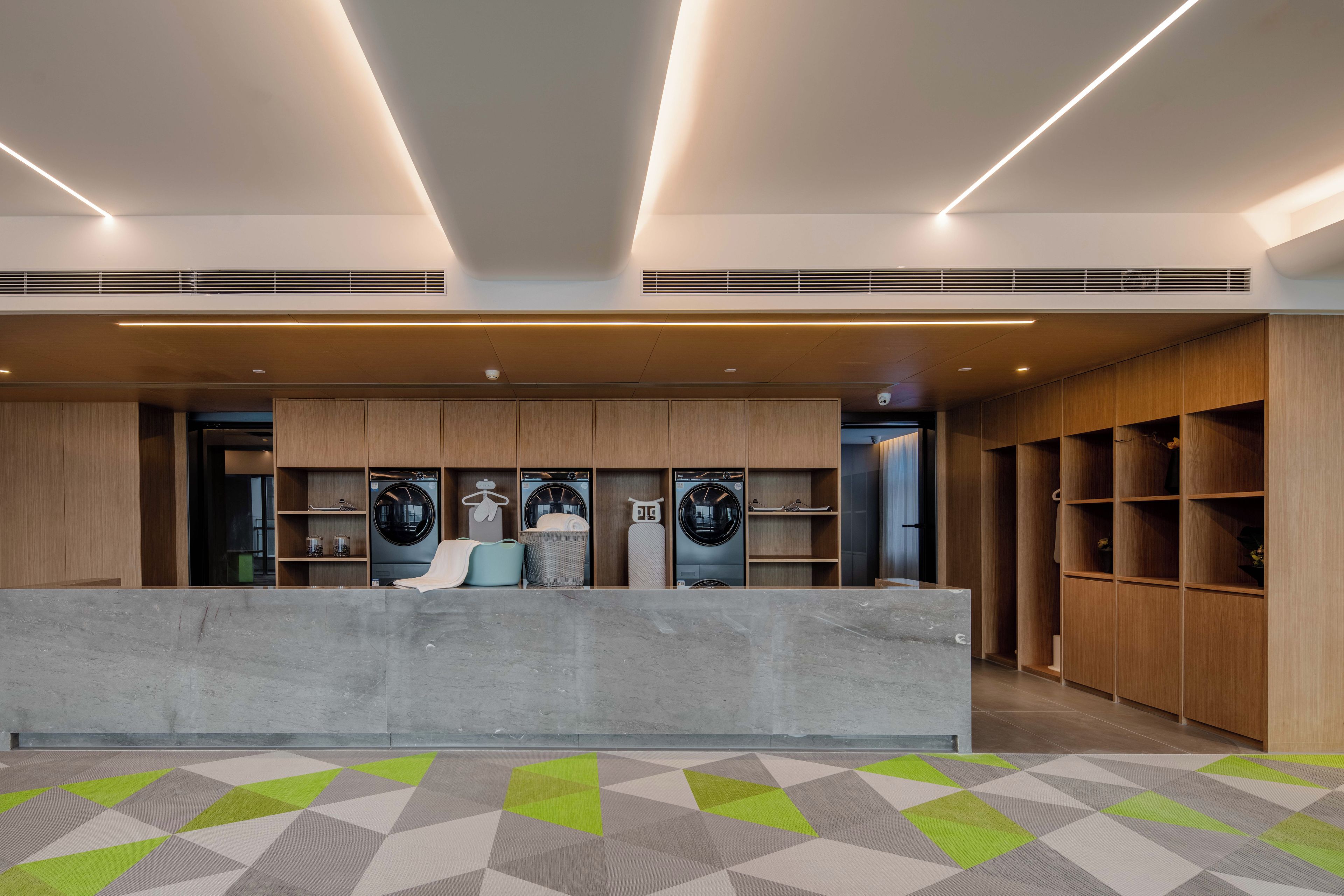 A modern reception area with a concrete counter, wooden shelving, and built-in laundry facilities.