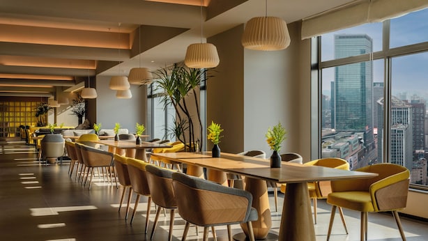A modern dining area with wooden tables and chairs, large windows with a city view, and hanging pendant lights. - Pagoda Design Hotel Chengdu Chunxiroad Taikoo Li (Chengdu)