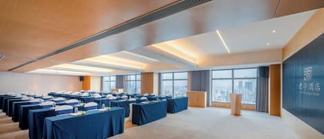 Un salón de conferencias con varias mesas, un atril y vistas a la ciudad a través de amplias ventanas.